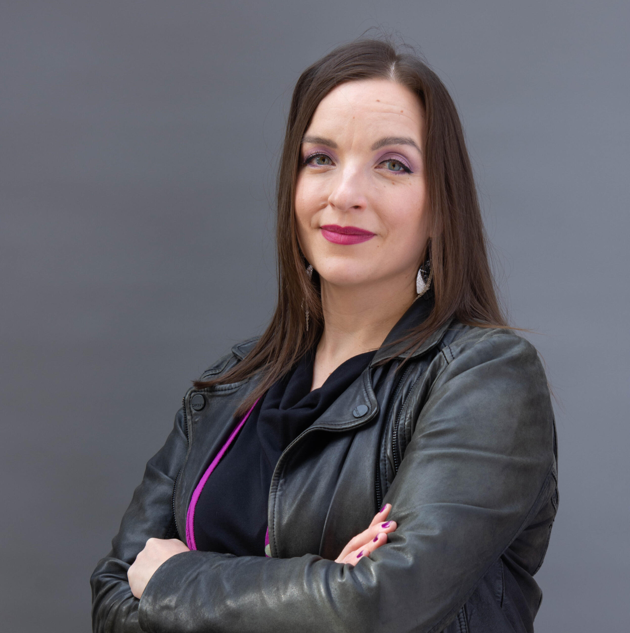 Nainen katsoo hymyillen kameraan. Kädet ovat ristissä.