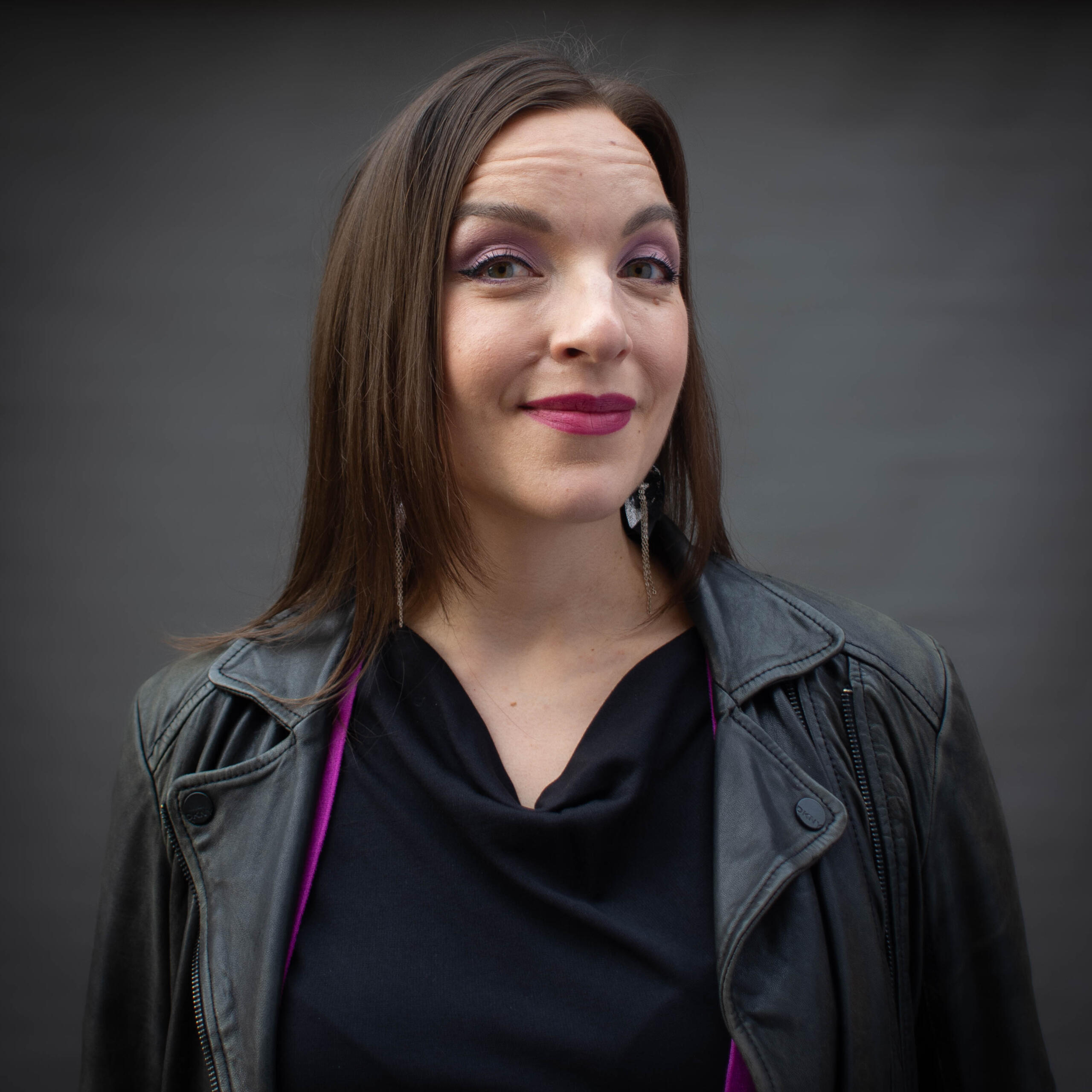 Nainen katsoo kameraan hymyillen. Hänellä on musta nahkatakki auki.